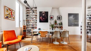 Ein modernes Wohnzimmer mit Essbereich, inklusive Bücherregal, einem großen Gemälde und einem leuchtend orangefarbenen Sessel.