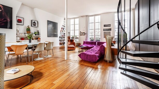 Ein geräumiges Wohnzimmer mit Holzboden, einem violetten Sofa, einer Essecke mit modernen Stühlen und einer Treppe mit schwarzer Geländer.