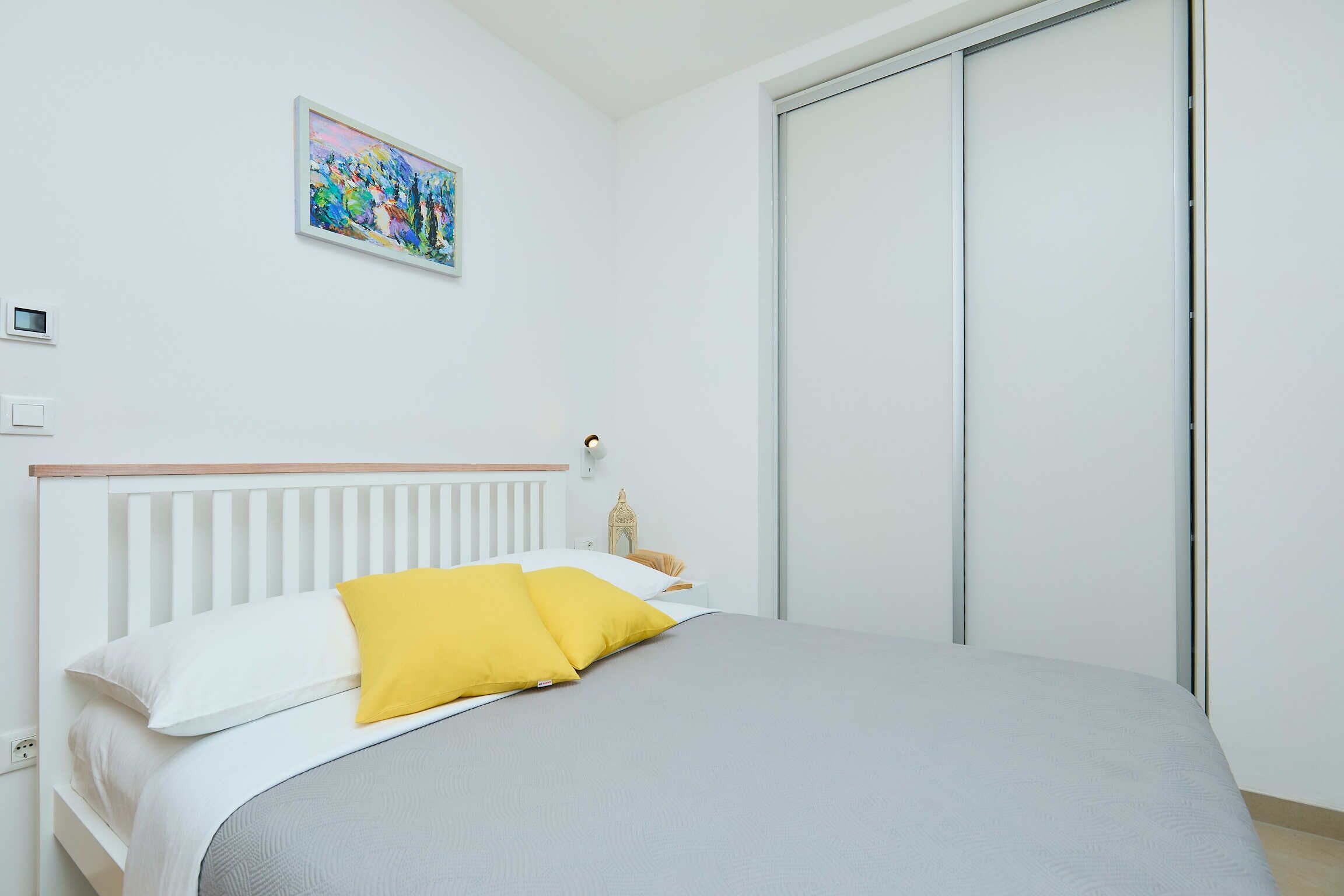 A neatly made bed with white and yellow pillows, a gray bedspread, and a white headboard.