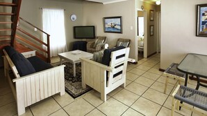 A cozy living room with a sofa, a small table, a TV, and a staircase.