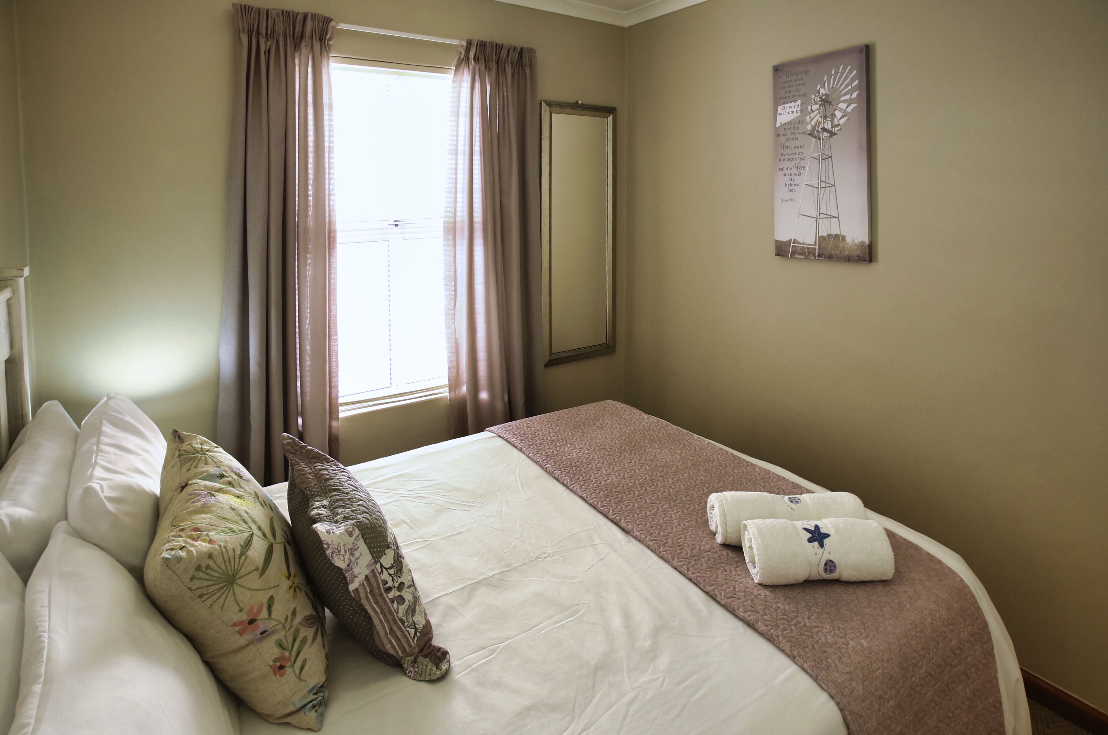 Habitació d'hotel amb llit, almoines, finestra amb cortines i una obra d'art penjada a la paret.