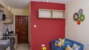 Un espacio habitable compacto con kitchenette, un sofá con cojines estampados, una mesita con un florero y una pared de acento roja.