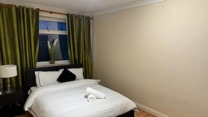 Un letto ben rifatto con lenzuola bianche, una testata scura e una tenda verde.