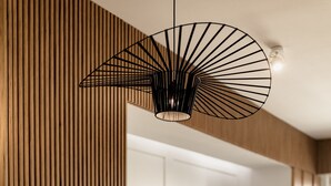 A modern dining area with a wooden table and quilted chairs, a black pendant light, and a wooden slatted wall. - Nest Inn Mirror Apartment (Cluj-Napoca)