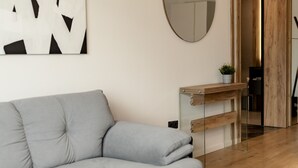 A modern living room with a grey sofa, a wooden coffee table, a round mirror, and a black pendant light. - Nest Inn Mirror Apartment (Cluj-Napoca)