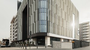 A modern building with a curved glass facade, a flat roof, and a parking area with bollards. - Nest Inn Mirror Apartment (Cluj-Napoca)