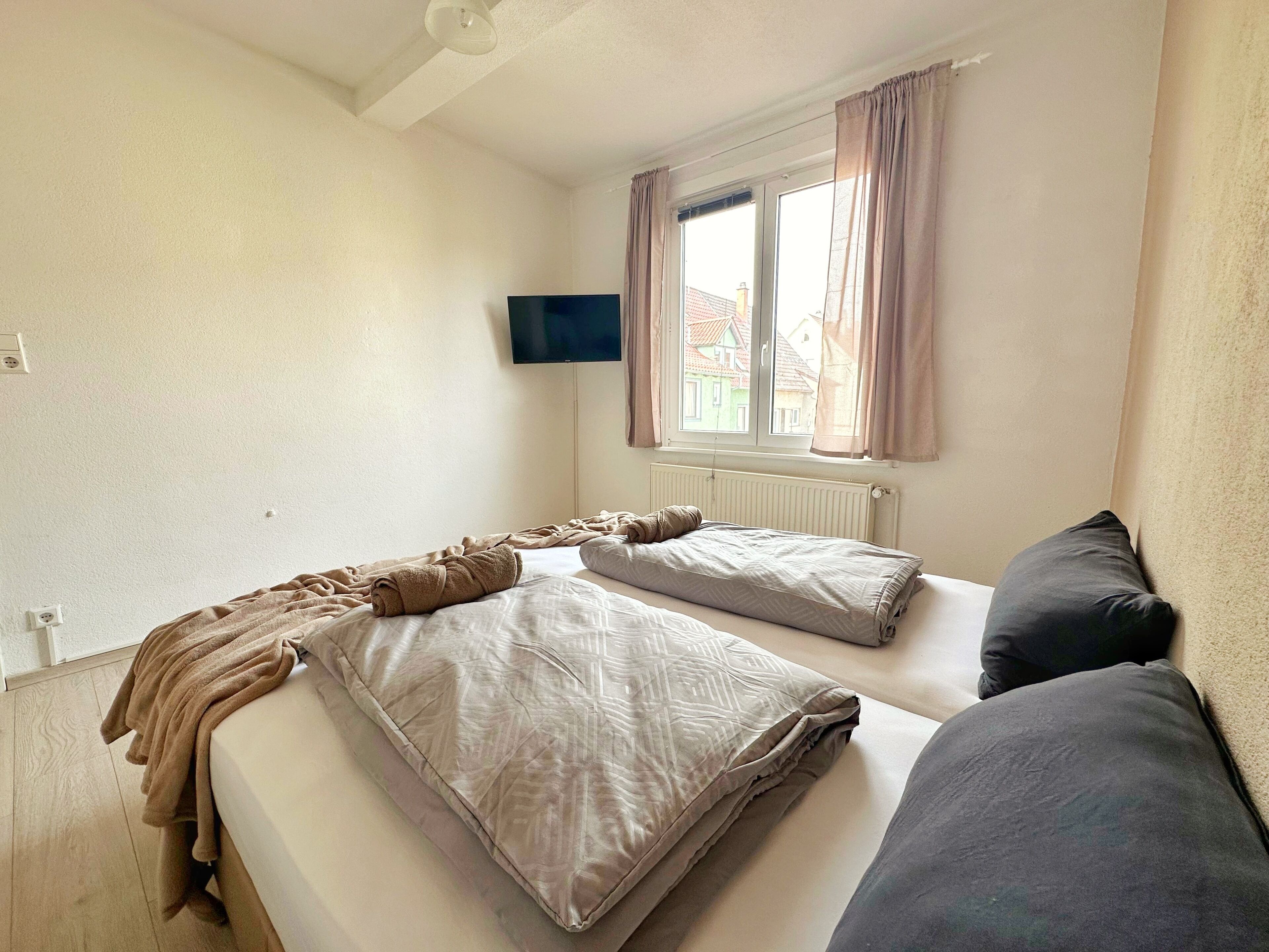 Une chambre avec deux lits, un téléviseur fixé au mur et une fenêtre avec des rideaux.