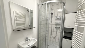 Ett modernt badrum med en dusch som är avskärmad med glasväggar, ett vitt handfat och en spegel ovanför.