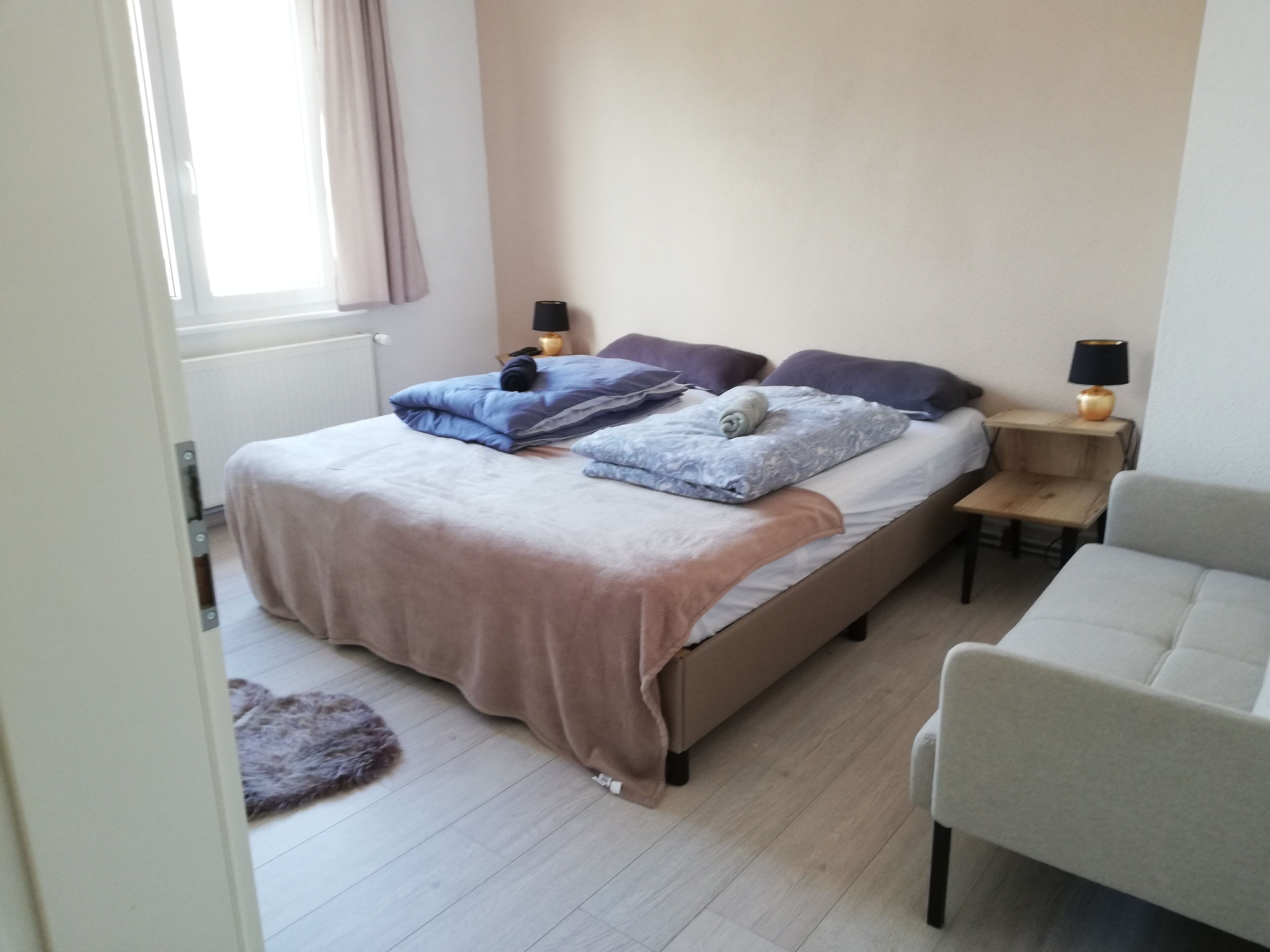 A bedroom with a bed, two bedside tables, a chair, and a window with curtains.