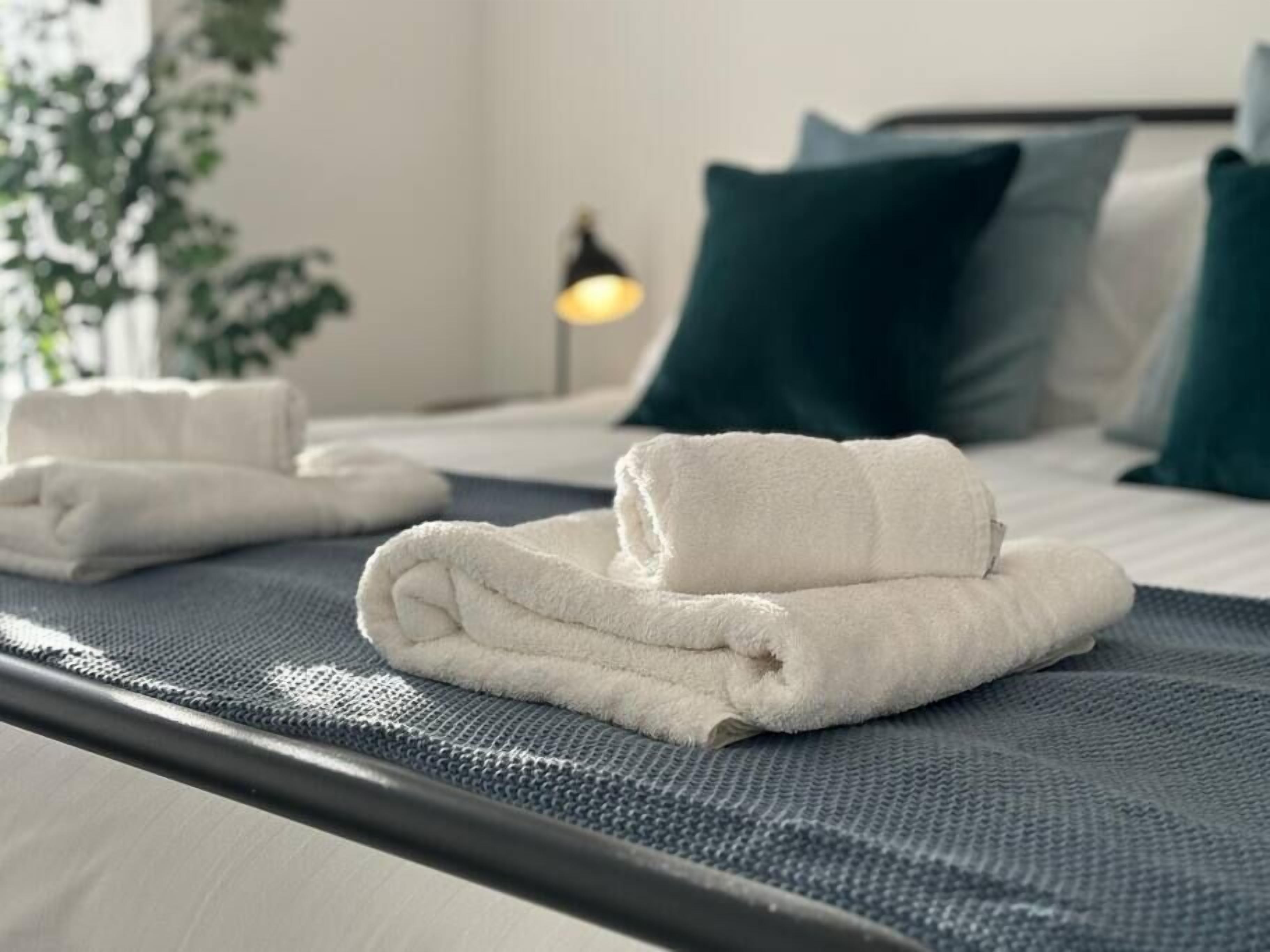 A neatly made bed with white towels folded on the side, a dark blue headboard, and a green pillow.