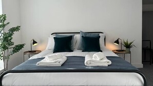 A neatly made bed with two pillows, a blue bedspread, and two towels folded on the bed. There are two bedside tables with lamps and a potted plant on one of them. - Shrewsbury House, 3 En-Suites (Shrewsbury)