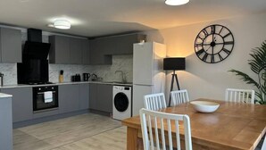 A modern kitchen with grey cabinets, a wooden dining table, and a black clock on the wall. - Shrewsbury House, 3 En-Suites (Shrewsbury)
