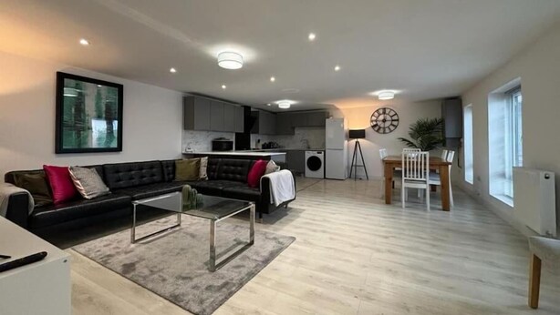 A modern living room with a black sofa, a glass coffee table, and a dining area with a wooden table and chairs. - Shrewsbury House, 3 En-Suites (Shrewsbury)