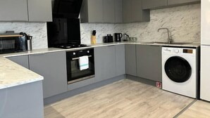 A modern kitchen with grey cabinets, a built-in oven, a stove, a sink, and a washing machine. - Shrewsbury House, 3 En-Suites (Shrewsbury)