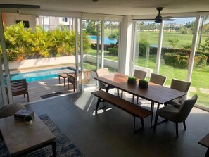 Un espace repas moderne avec vue sur la piscine, de grandes fenêtres et une vue sur un terrain de golf.