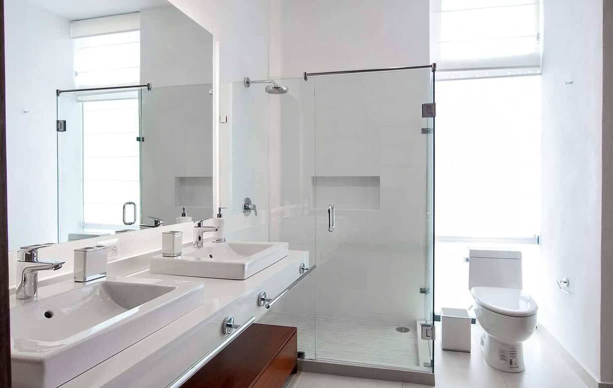 A modern bathroom with two sinks, a glass shower enclosure, and a toilet.
