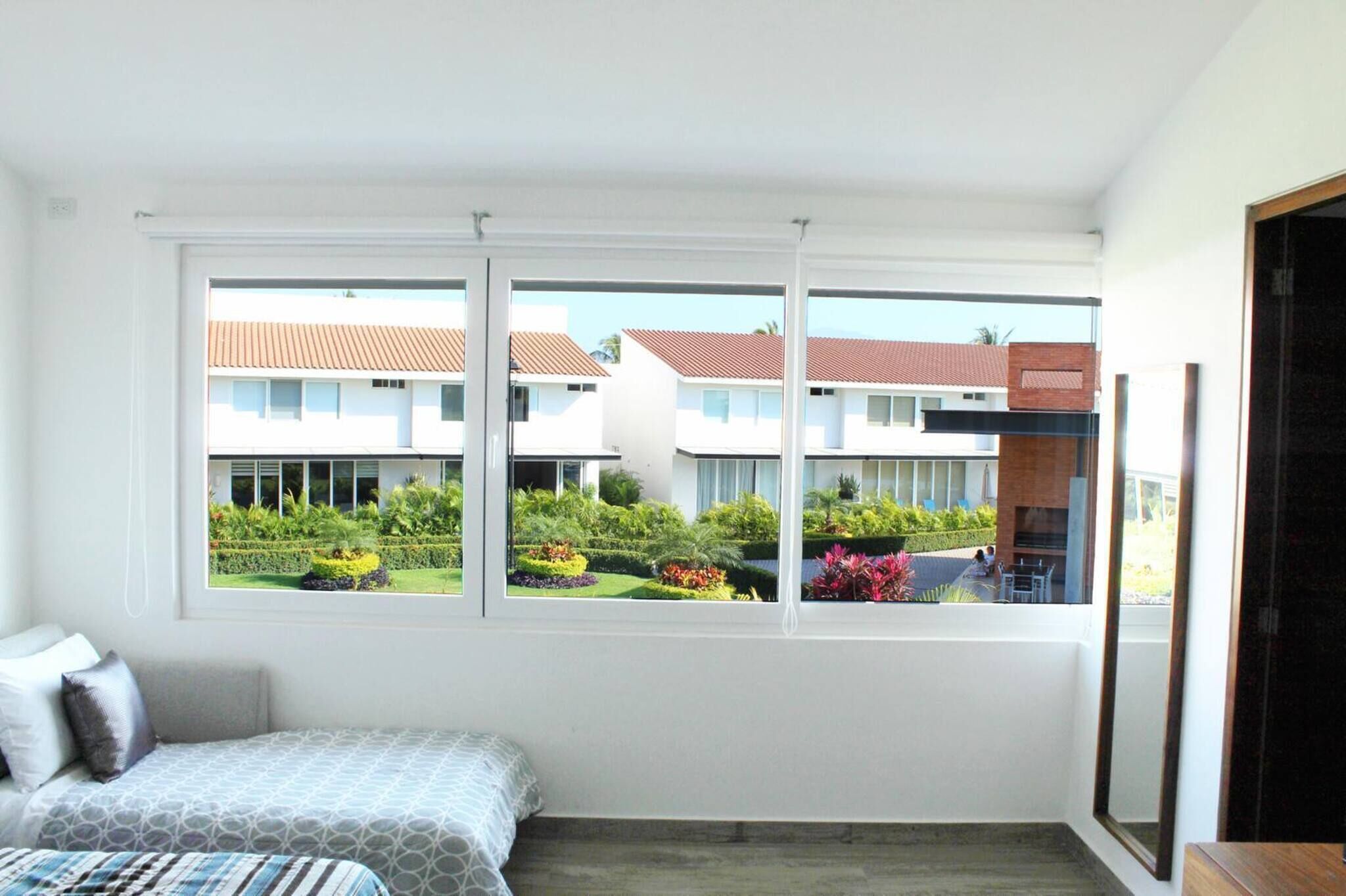 A bedroom with a bed, a window, and a view of a building with a garden.