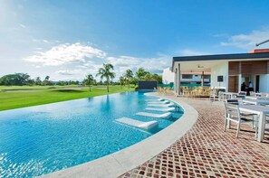 Una piscina con acqua cristallina, un patio in mattoni e un edificio moderno con posti a sedere all'aperto.