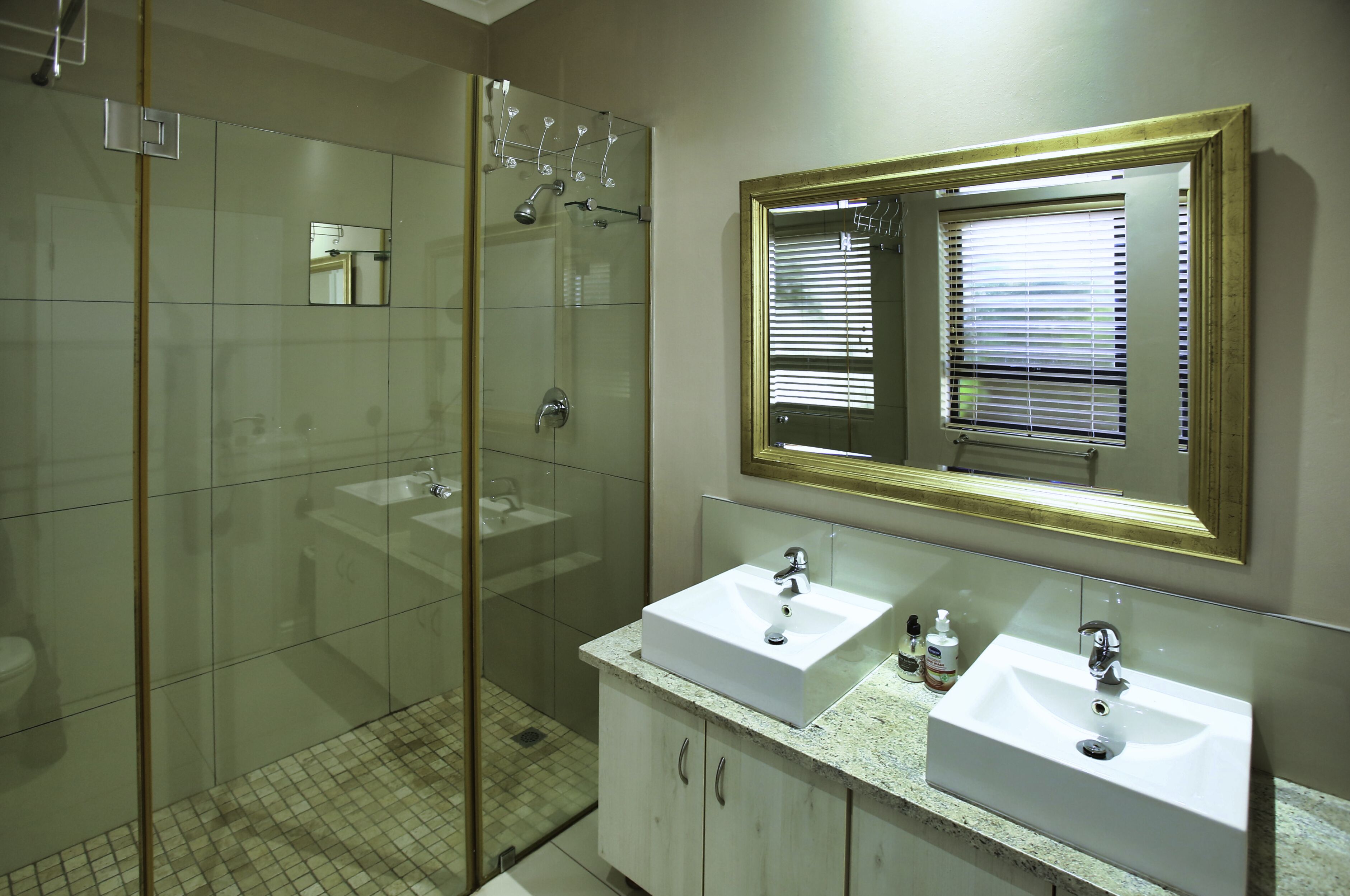 A bathroom with two sinks, a glass shower enclosure, and a large mirror with a gold frame.