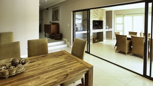 A dining area with a wooden table and chairs, a bowl of decorative items, and a view of a kitchen and dining room through glass doors.