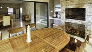 A modern kitchen with a built-in oven, a dining area with a wooden table and wicker chairs, and a staircase leading to an upper level.
