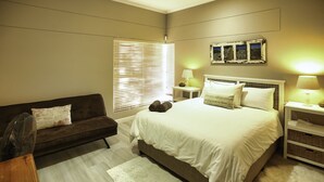 A bedroom with a bed, a sofa, a small table, and a lamp.