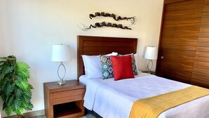 A bedroom with a wooden headboard, a bed with white bedding and a yellow throw, a nightstand with a lamp, and a potted plant.