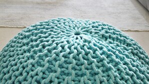 A living room with a grey sofa, a coffee table, and a knitted pouf.