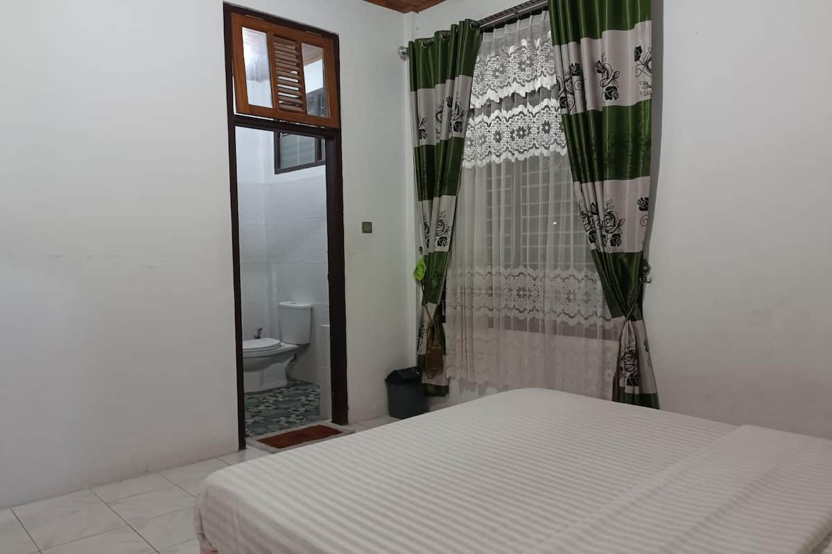 A bedroom with a bed, a window with green and white curtains, and a view of a bathroom.
