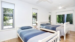 A room with two single beds, a ceiling fan, and large windows with blinds. - Russell Street Retreat (Hawks Nest)
