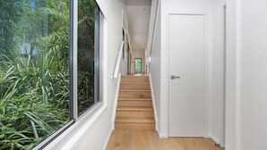 Un pasillo estrecho con suelo de madera, paredes blancas y una ventana de vidrio a la izquierda.