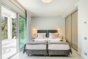 Une chambre avec deux lits, une grande porte-fenêtre coulissante donnant sur un balcon et une vue sur les arbres.