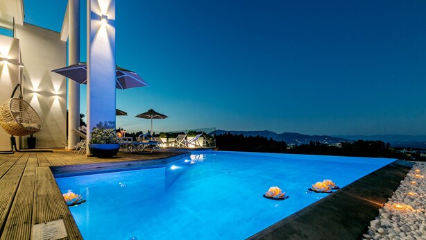 Una piscina con muelle de madera, sillas de descanso, sombrillas y vistas a las montañas.