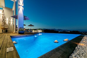 Une piscine avec une terrasse en bois, des chaises longues, des parasols et une vue sur les montagnes.
