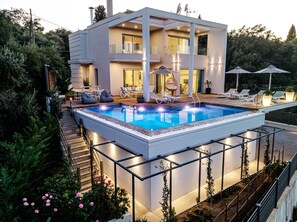 Une maison moderne à deux étages, dotée d’une piscine, d’un espace extérieur aménagé et d’un patio bien éclairé.
