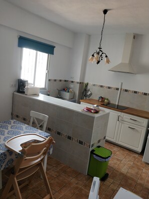 Een compacte keuken met een eethoek, een koffiezetapparaat, een spoelbak en een groene prullenbak.