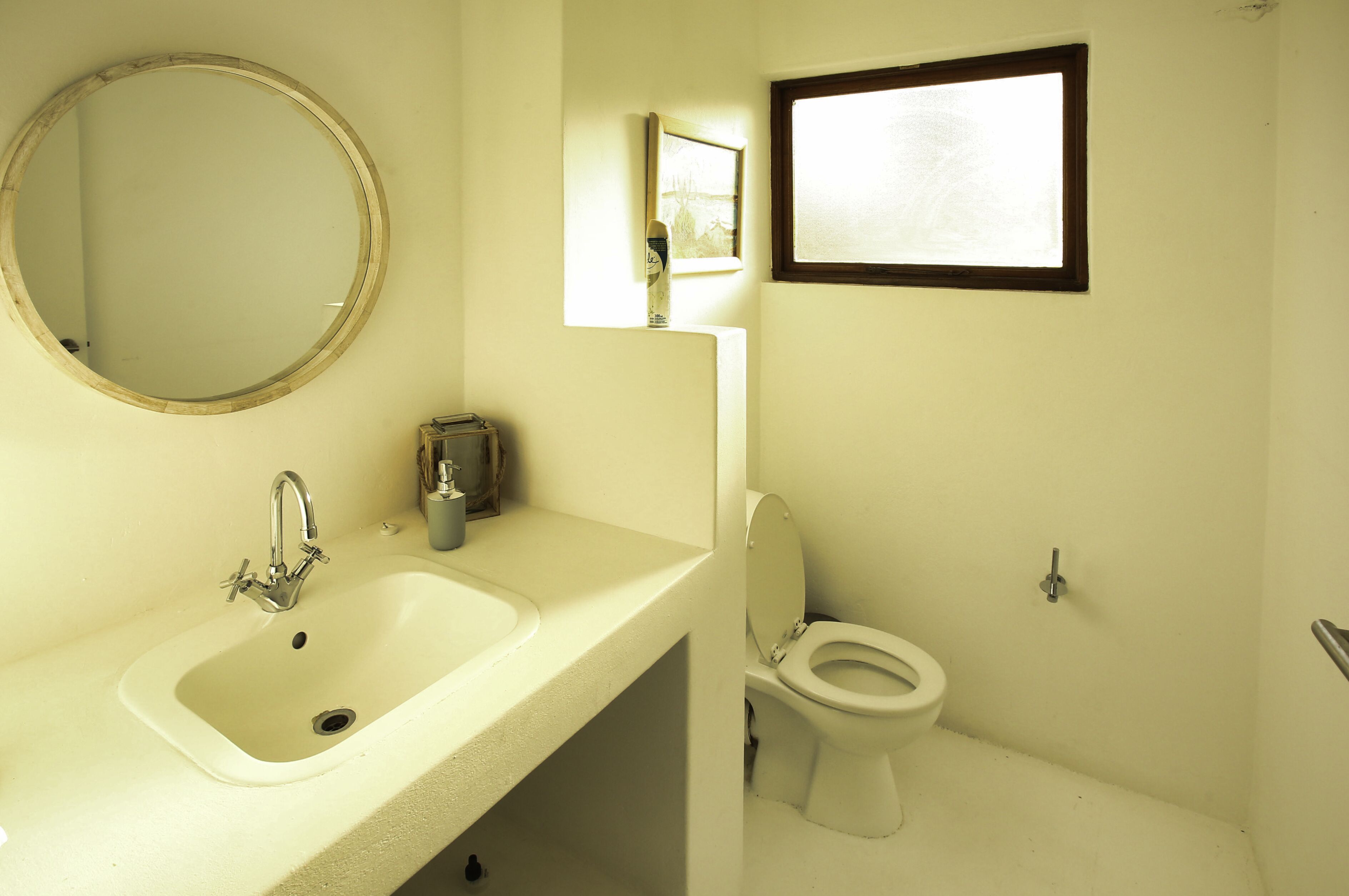 A bathroom with a sink, mirror, toilet, and a window.