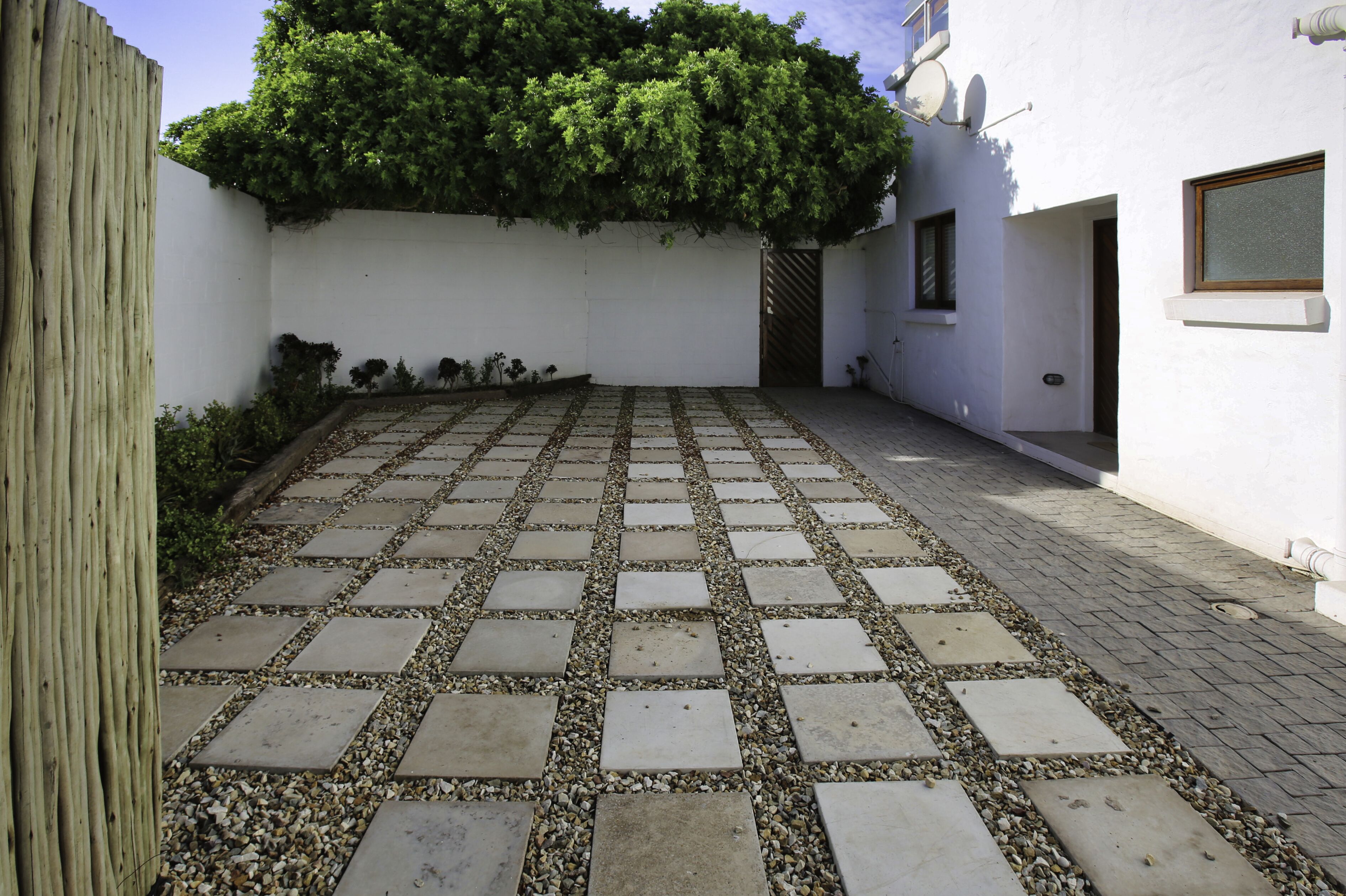A paved courtyard with a white wall and a wooden fence on one side.