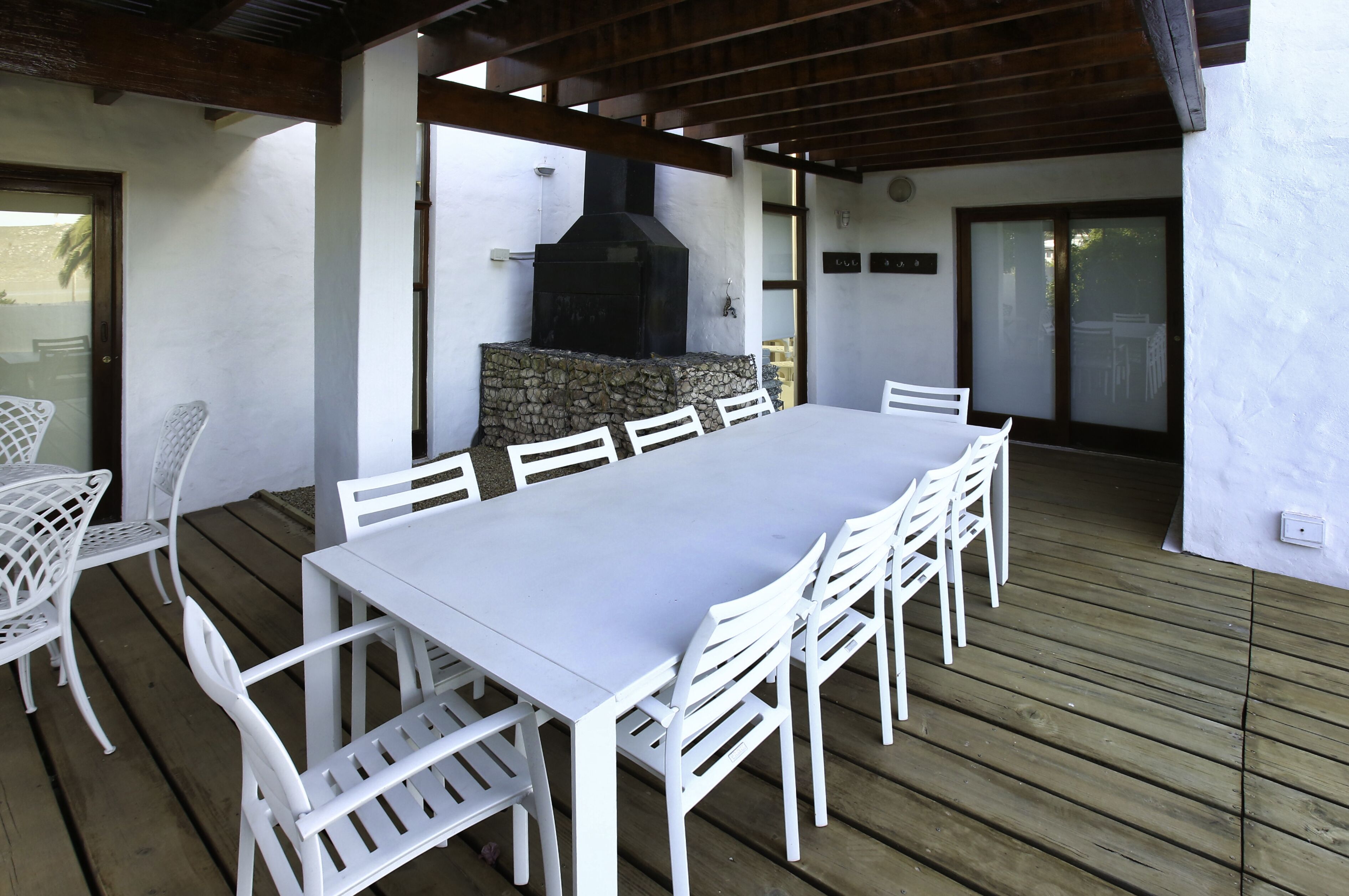 Une terrasse extérieure avec une table et des chaises blanches, un mur en pierre et un barbecue noir.