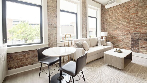 Un salon moderne avec un mur en briques, un canapé blanc, une table ronde et deux chaises noires.