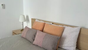 A neatly made bed with striped bedding, a bedside lamp, and three pillows of varying textures and colors. - Apartamento T1 em Quarteira! (Quarteira)