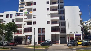 A multi-story white building with balconies, a visible entrance, and a sign for 'BATALHA'. - Apartamento T1 em Quarteira! (Quarteira)