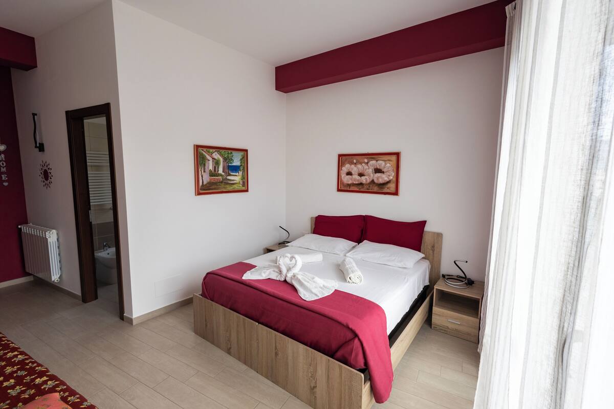 A bedroom with a wooden bed, white bedding, red pillows, and two wall-mounted paintings.