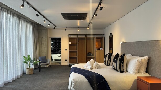 A modern hotel room with a large bed, a bedside table, a wardrobe, and a bathroom visible through an open door. - Neighbourgood Loop (Cape Town)