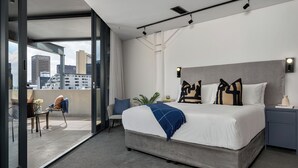A modern hotel room with a large bed, a desk, and a view of the cityscape through floor-to-ceiling windows. - Neighbourgood Loop (Cape Town)