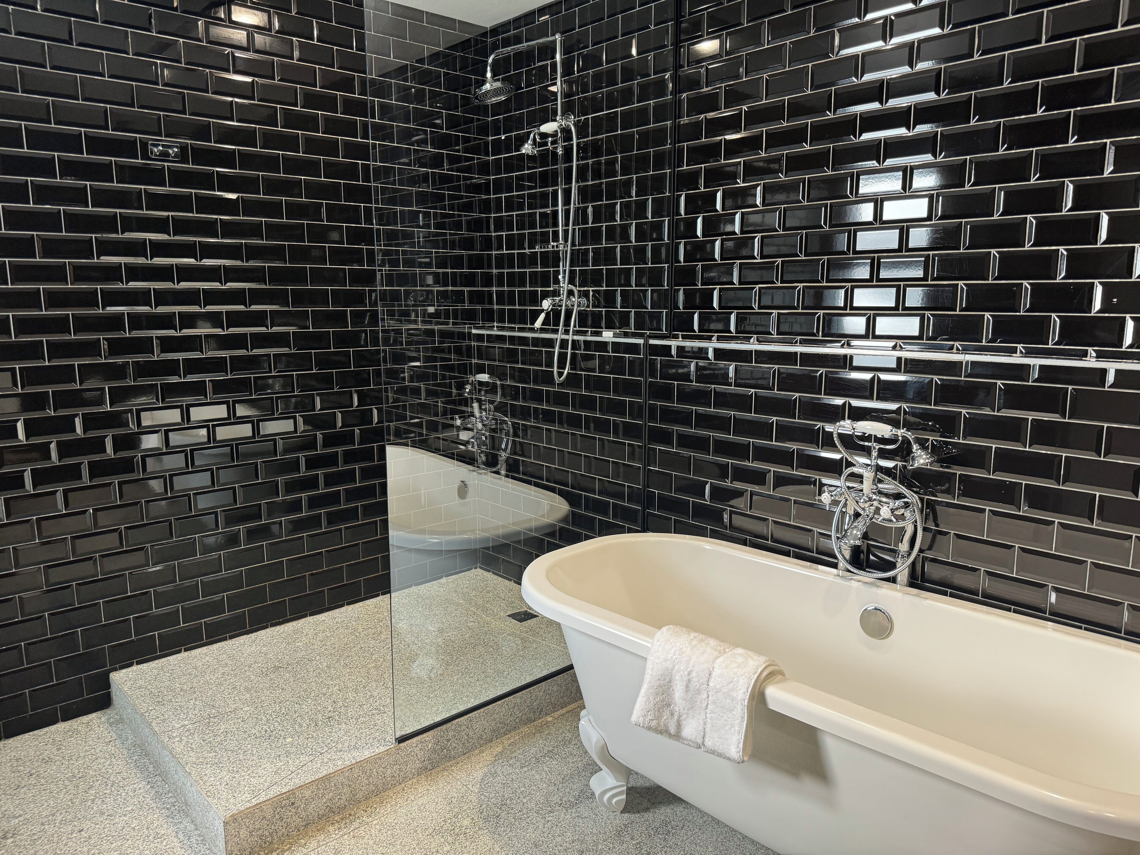 A bathroom with black tiled walls, a white bathtub, and a separate sink.