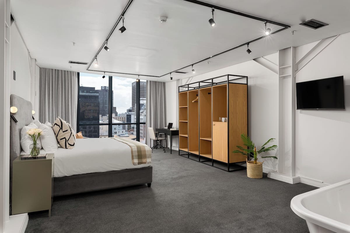 Quarto de hotel moderno com uma cama grande, uma escrivaninha, um guarda-roupa e vista para a cidade.