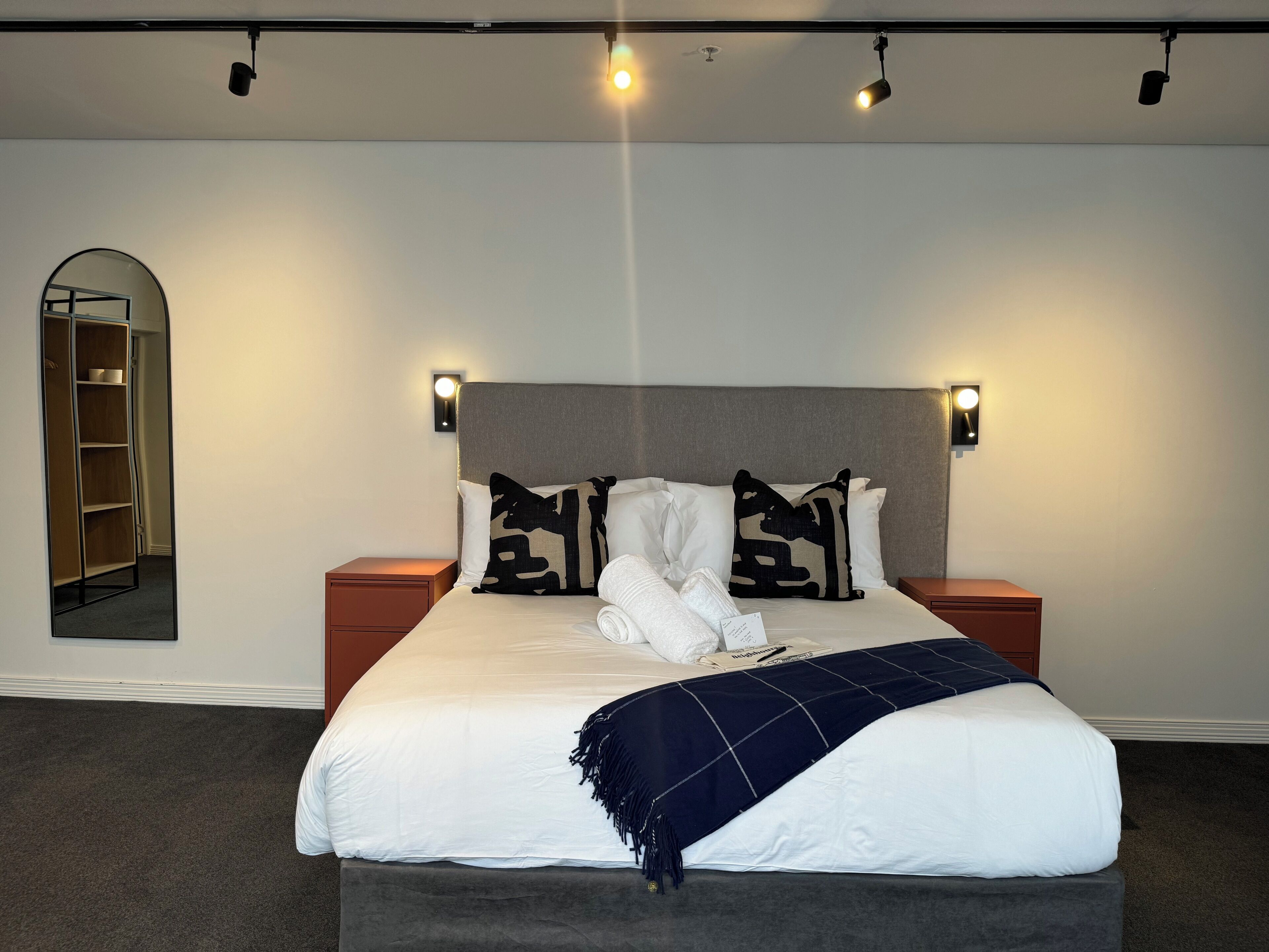 A neatly made bed with a headboard, two bedside tables, and a wall-mounted light fixture.