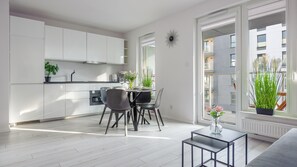 Eine moderne Küche mit weißen Schränken, ein Essbereich mit zwei Stühlen und einem kleinen Tisch. Auf der Küchenarbeitsplatte steht ein Blumentopf und auf dem Esstisch ebenfalls.