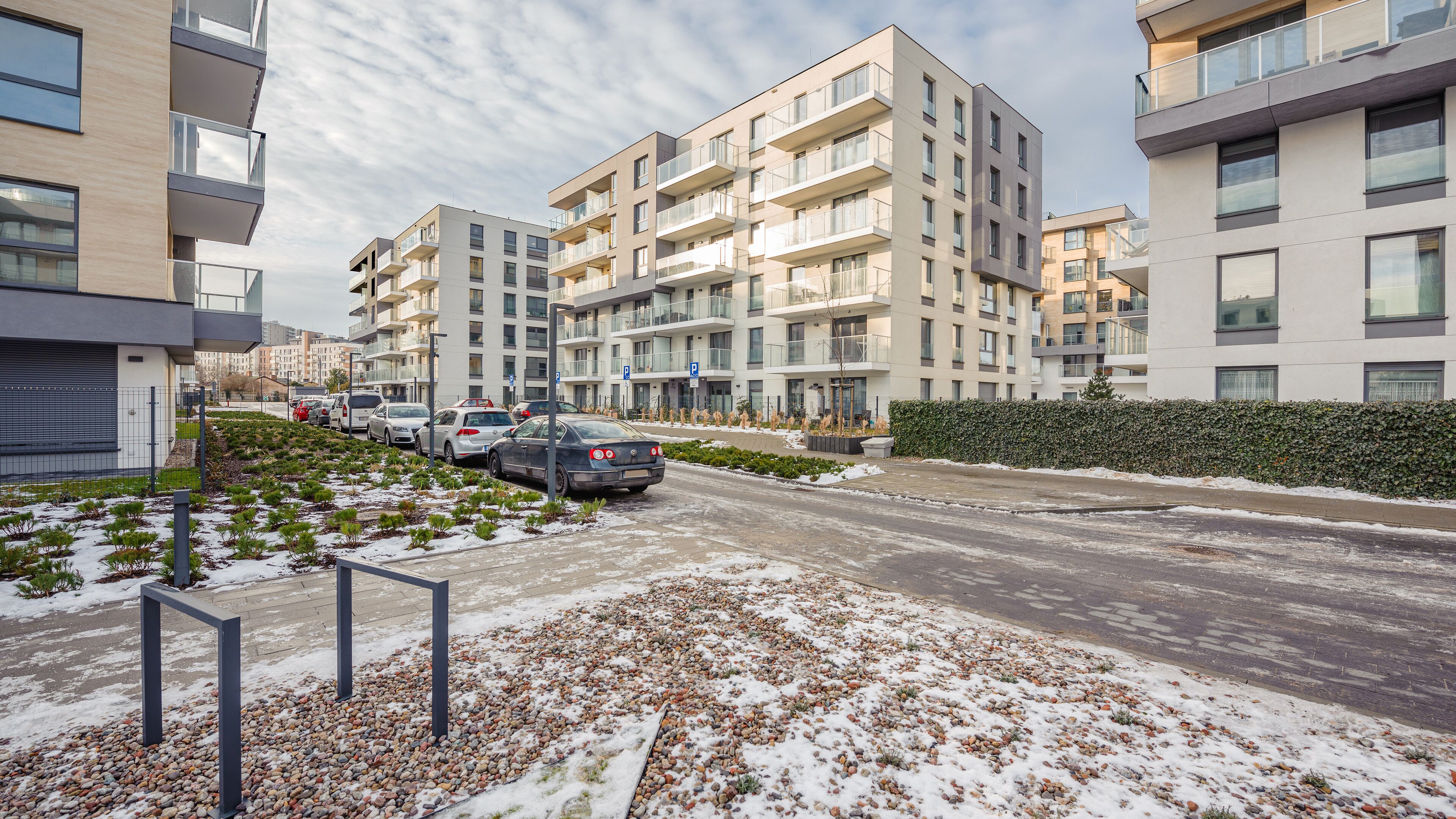 A modern apartment building with multiple balconies, a parking area, and a snow-covered ground.